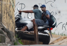 An alleged drug trafficker aims a weapon while escaping in a motorcycle at the Complexo do Alemao in Rio de Janeiro, Brazil, Saturday, Nov. 27, 2010. Occasional gunfire broke the tense stillness Saturday morning as armored vehicles prepared to push past barriers into Rio's most dangerous slum, as police increased pressure on drug traffickers believed to have ordered the wave of violence that has terrorized the city this week. (AP Photo/Felipe Dana)